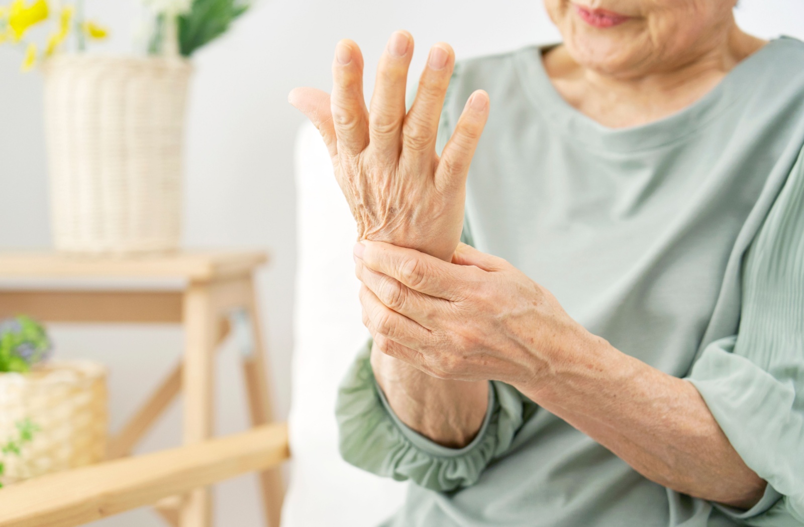An older adult sitting at home and rubbing their wrist to relieve joint pain.