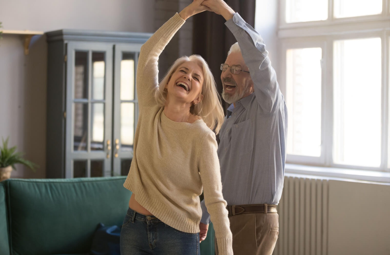 An older adult laughs while their spouse spins them during an impromptu dance in their living room in senior living