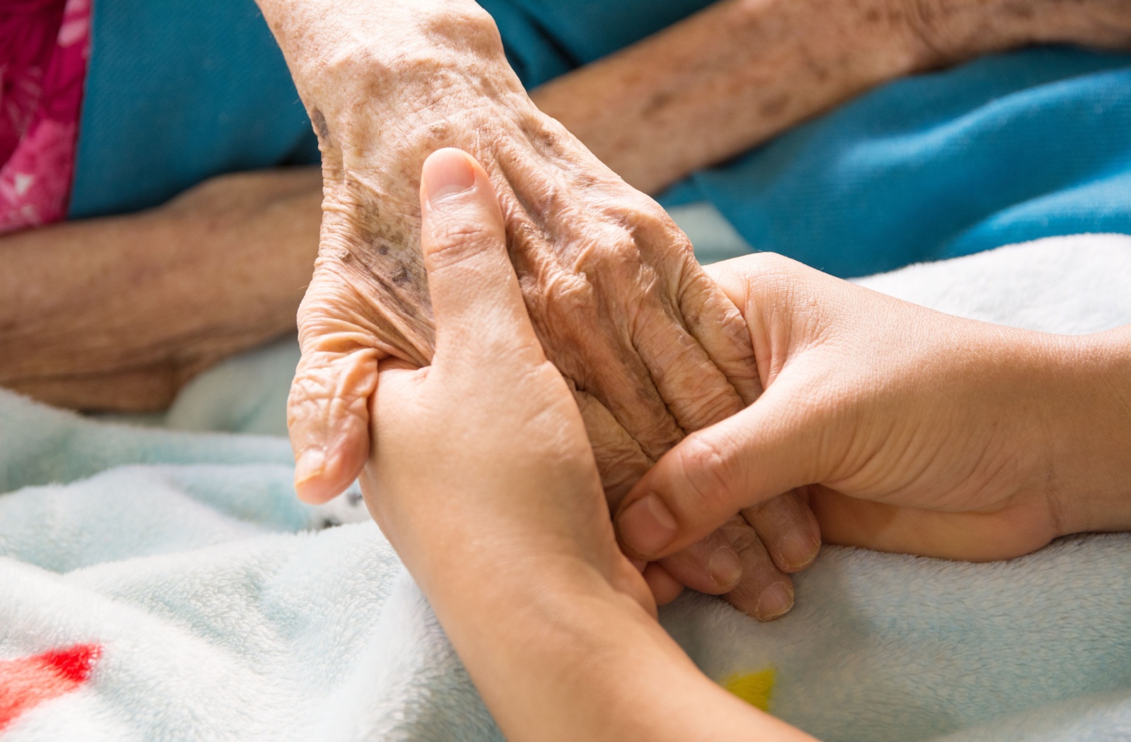 A close-up image of a caregiver holding an older resident's hand in senior living