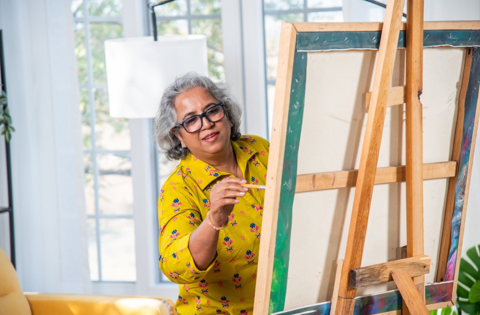A senior paints on a canvas propped up on an easel in a well-lit senior living community.
