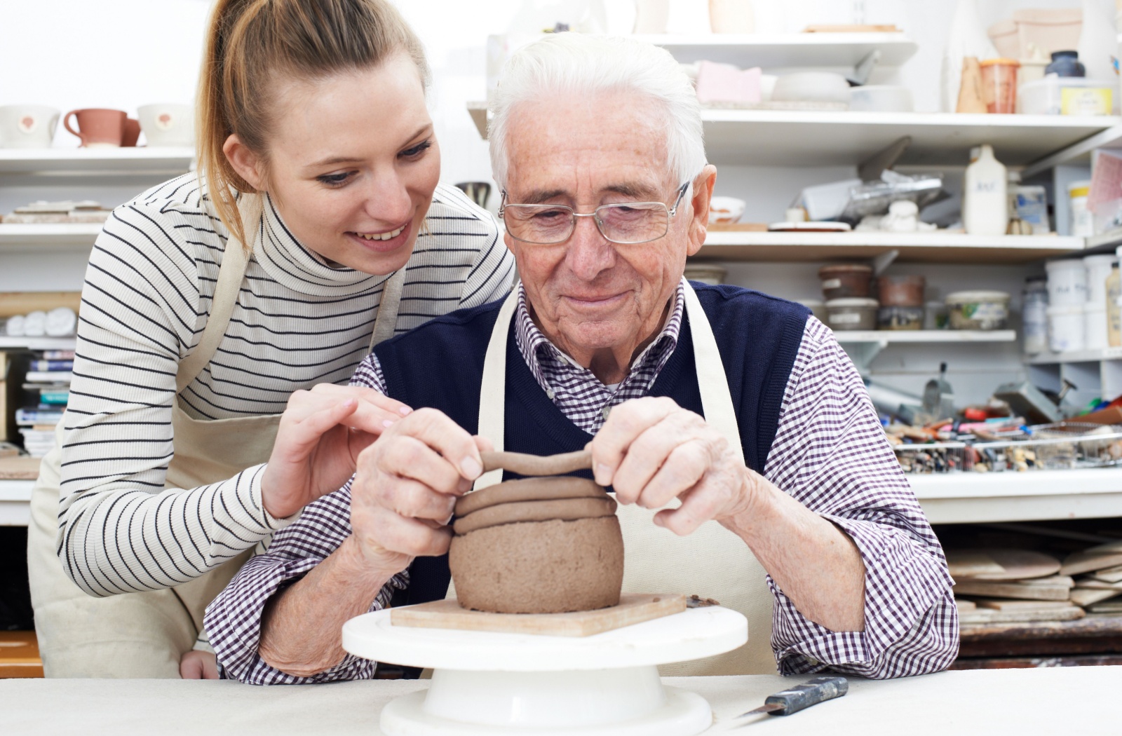 An instructor assists a senior with creating a piece of pottery.