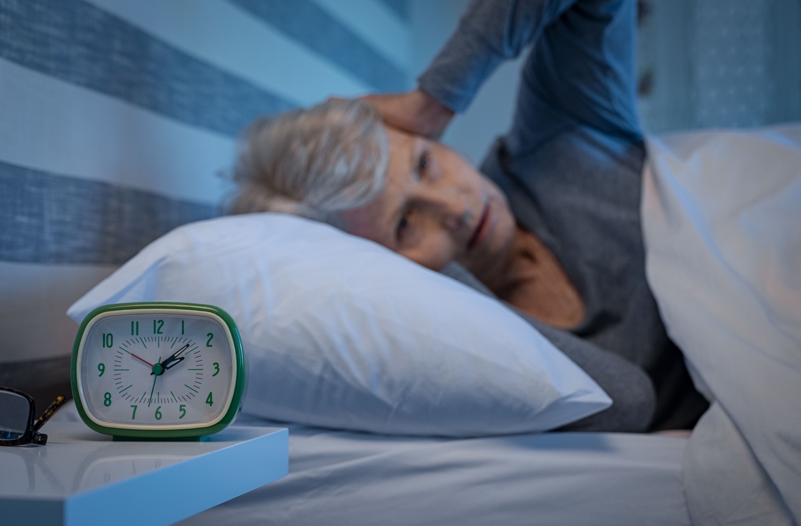 A senior lies in bed experiencing insomnia while a clock reads 2:08am.